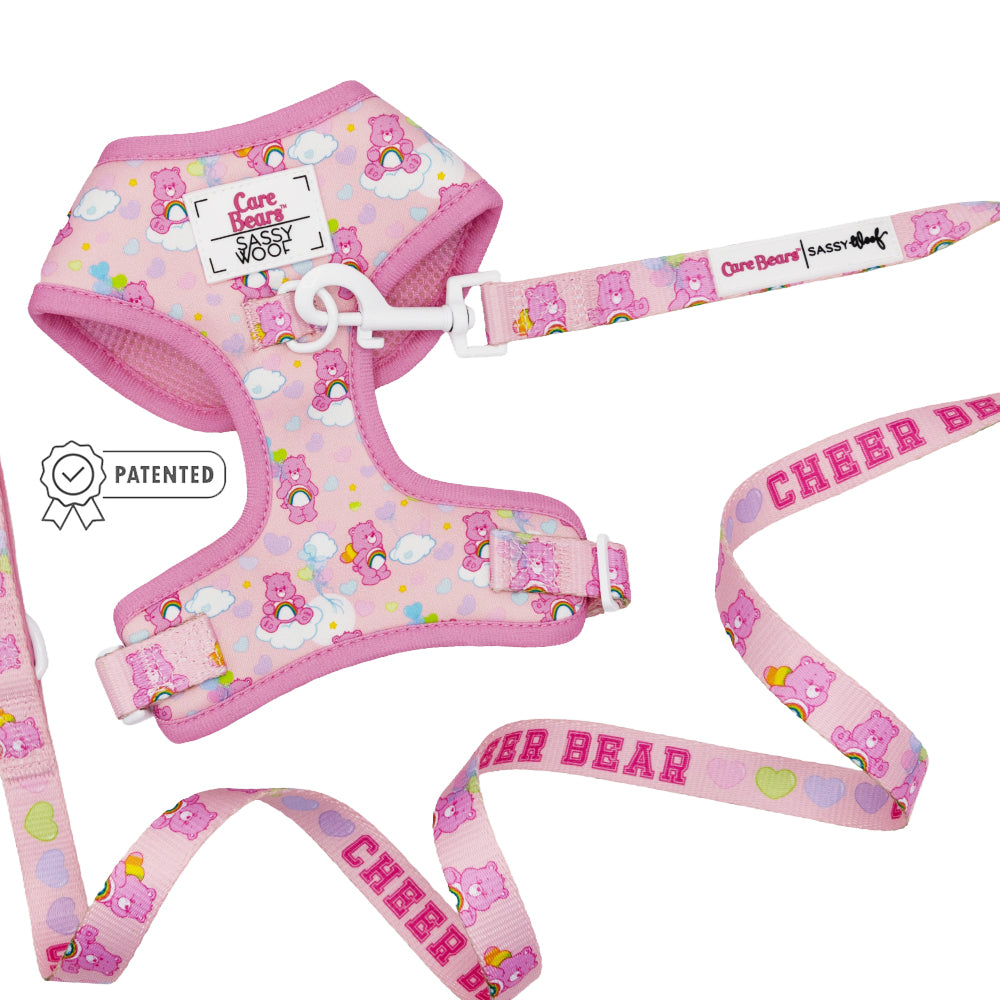 The Sassy Woof Dog Two Piece Bundle - Care Bears™ Cheer Bear includes an adjustable harness with Cheer Bear and heart designs, a Sassy Woof label, and a matching leash reading CHEER BEAR in bold pink plus a patented badge icon.