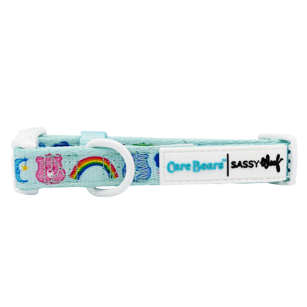 The Sassy Woof Dog Collar - Care Bears™ Care-a-Lot is a light blue, adjustable neoprene collar with rainbow designs, a white buckle, Sassy Woof tags, and a white D-ring for leash attachment.