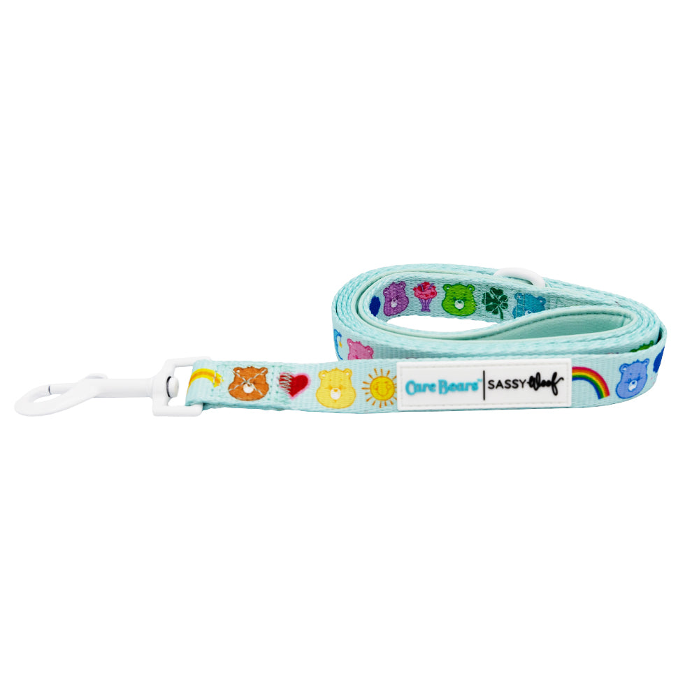 The Dog Leash - Care Bears™ Care-a-Lot by Sassy Woof is light blue with colorful Care Bears faces, hearts, stars, and rainbows. It features a white clip and labels reading "One Beard" and "Sassy Woof.