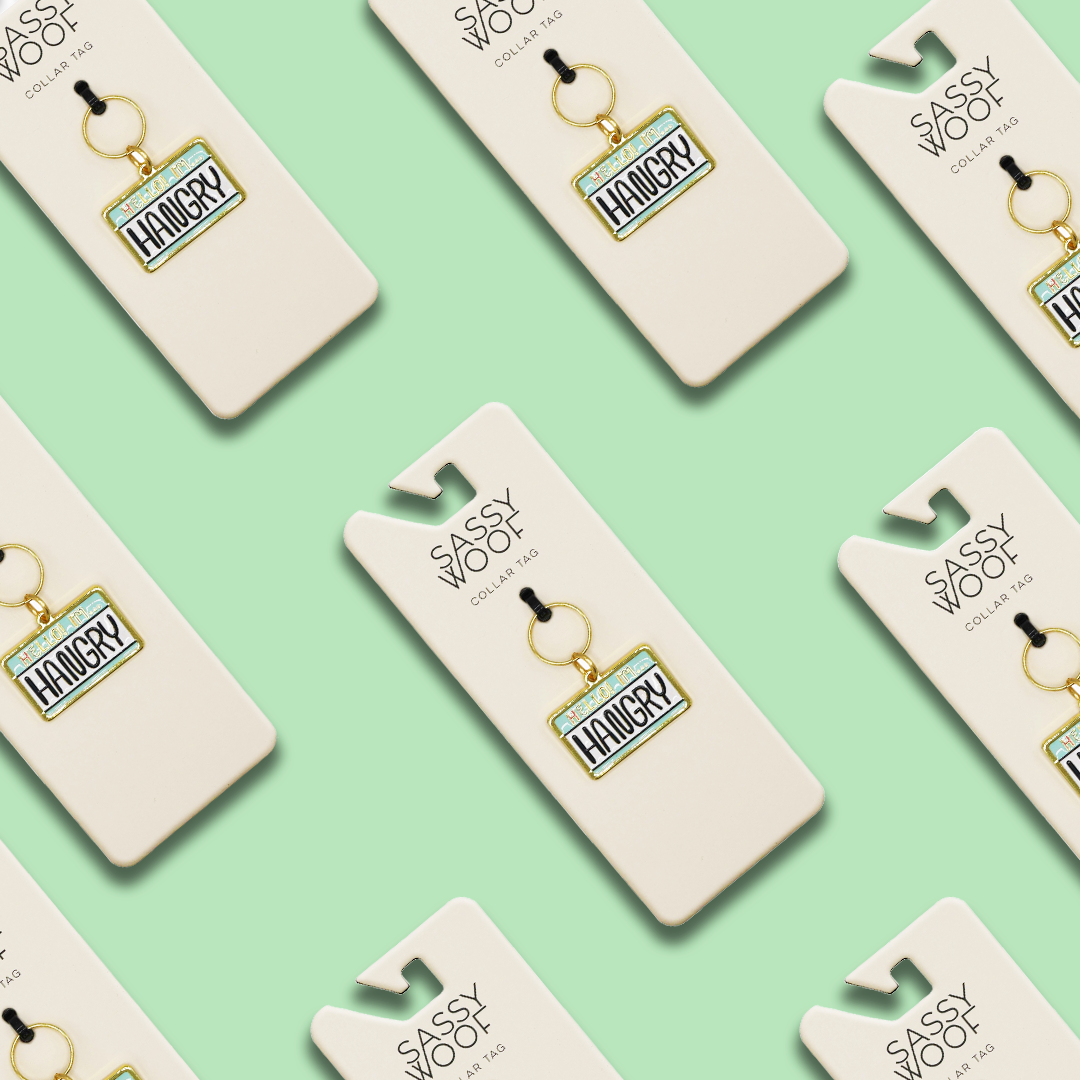 Multiple "Collar Tag - Hello I'm Hangry" tags by Sassy Woof are displayed on white Sassy Woof cards, arranged diagonally in a repeating pattern against a mint green background.