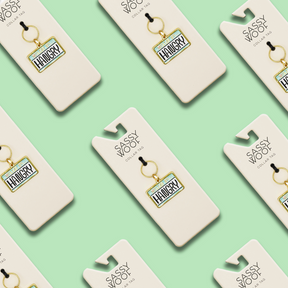 Multiple "Collar Tag - Hello I'm Hangry" tags by Sassy Woof are displayed on white Sassy Woof cards, arranged diagonally in a repeating pattern against a mint green background.