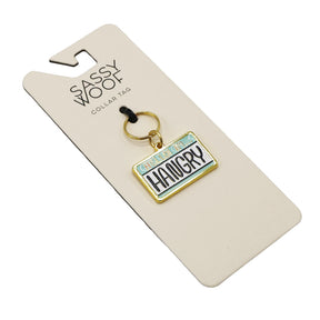 The Sassy Woof Collar Tag - Hello I’m Hangry is a gold dog tag on a branded card, styled like a license plate and boldly stating CAUTION: HANGRY—perfect for pups with personality.