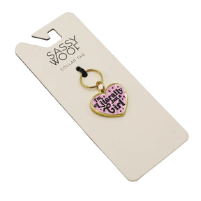 The Sassy Woof Collar Tag - Just a Girl is a heart-shaped tag with a pink background, gold accents, and "I'm Literally a Girl" text. It comes on a keyring and is displayed on branded Sassy Woof packaging.