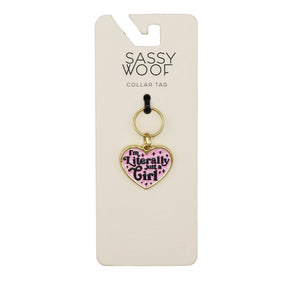 The Sassy Woof Collar Tag - Just a Girl is a pink, heart-shaped dog tag with gold accents and "Im Literally Just a Girl" in black, attached to a keyring and displayed on branded packaging.