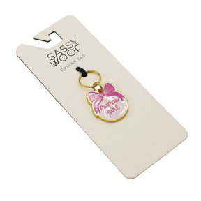 The Sassy Woof Collar Tag - Mama's Girl features a gold edge, pink bow, and "mama’s girl" in pink on white—adding a stylish, charming touch to your pup’s collar. Attached to a branded Sassy Woof card.