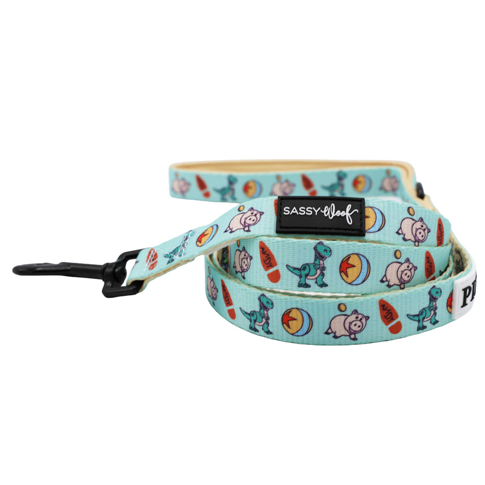 The Dog Leash - Disney and Pixar's Toy Story by Sassy Woof features colorful cartoon dinosaurs, pigs, and bones, plus a black clip and label—a playful blue leash for your Disney-loving pup.