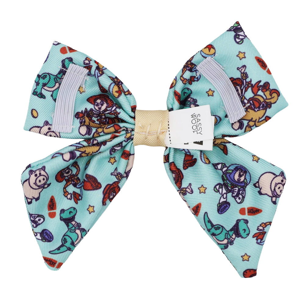 The Sassy Woof Dog Sailor Bow – Disney and Pixar's Toy Story features a light blue design with colorful cartoon characters, stars, and shapes. Finished with a beige center band, it brings playful Toy Story style to your pup's look.