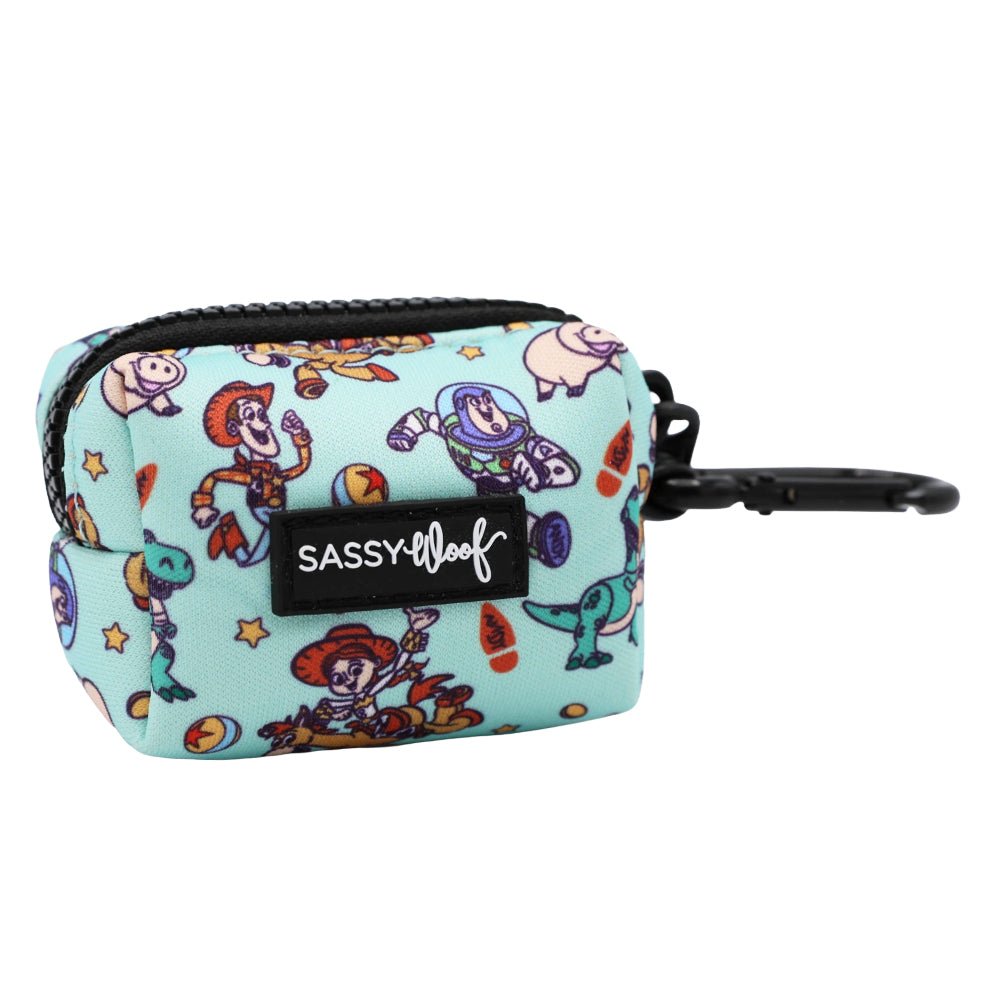 The Sassy Woof Dog Waste Bag Holder - Disney and Pixar's Toy Story features a light blue pouch with cartoon characters, stars, a black zipper, and clip. This handy pouch has a front SASSY WOOF label and is perfect for holding dog waste bags.