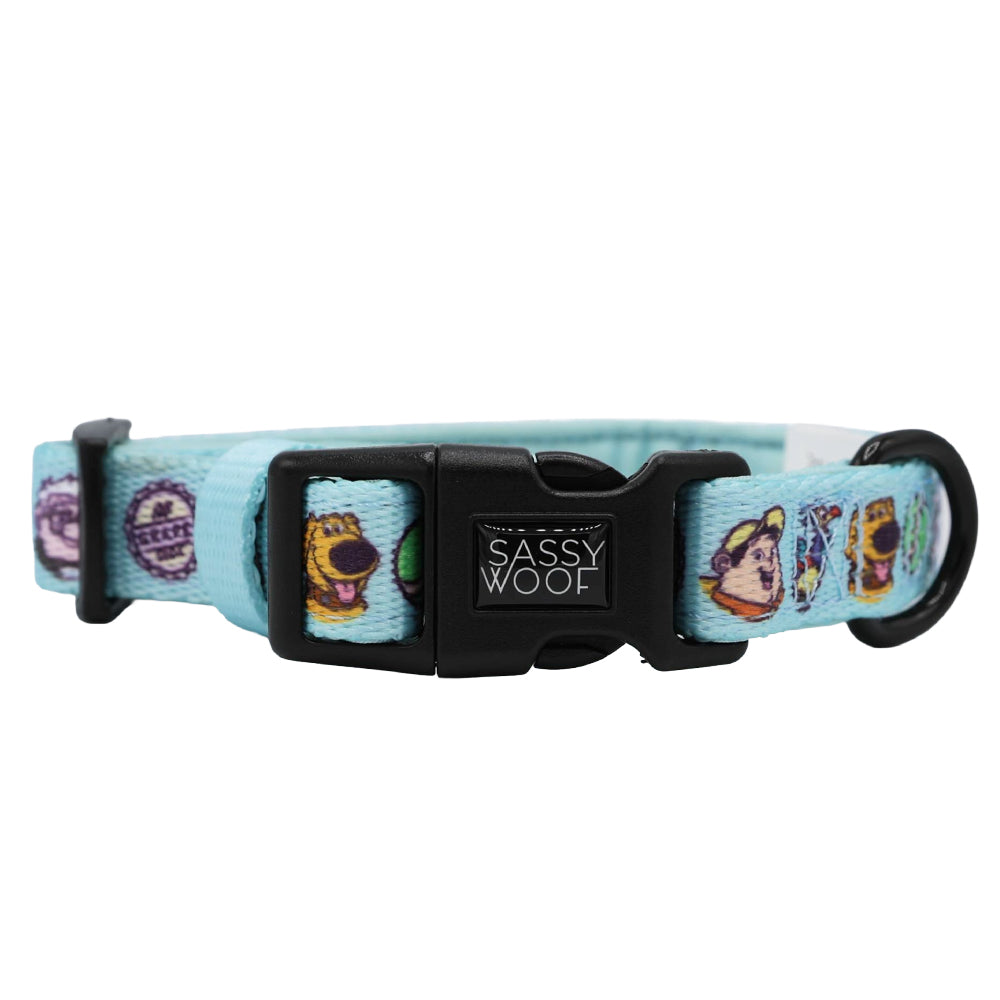 The Sassy Woof Dog Collar - Disney and Pixar's Up features a light blue design with cartoon dog faces, a black buckle, logo clasp, and black D-ring for leash attachment. Pair with an adjustable harness for a comfy, coordinated look.