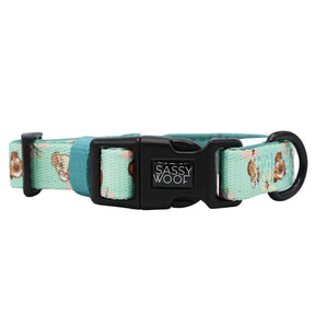 Introducing the Dog Four Piece Bundle - Disney’s The Lion King Wild Kingdom by Sassy Woof: a mint green dog collar from the exclusive Lion King pet collection, adorned with floral and dog face patterns, designed with a sturdy black plastic buckle marked “Sassy Woof,” and equipped with a metal ring for easy leash attachment.