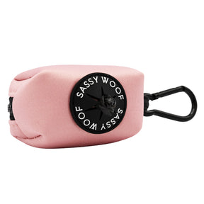The Sassy Woof Dog Waste Bag Holder in Dusty Rose is a blush pink fabric accessory with a black zipper, clip, and a round rubber Sassy Woof label.