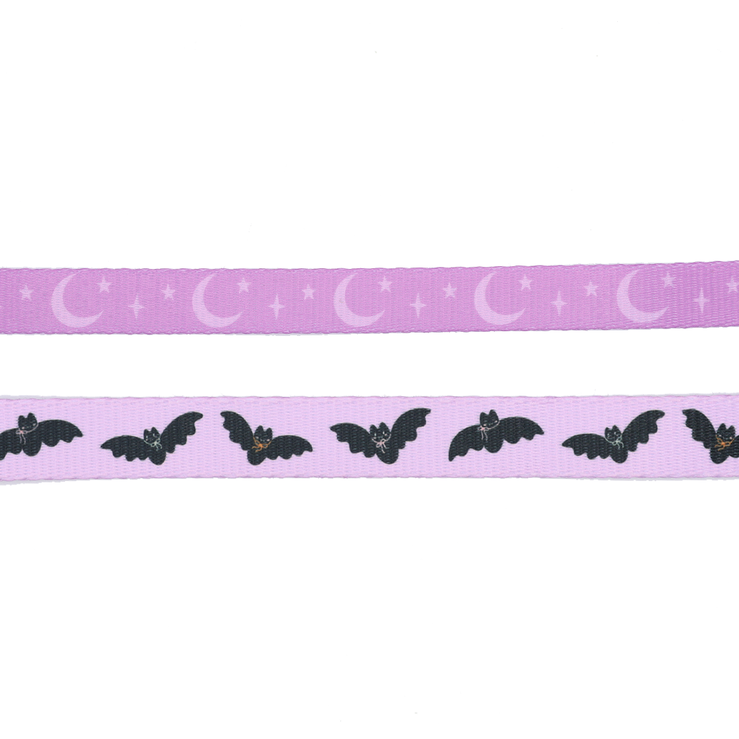 Two strips of purple ribbon evoke the enchanting look of the Sassy Woof Dog Leash - Lil Batty: the top showcases crescent moons and stars, reminiscent of a dreamy autumn night, while the bottom displays black bats with white eyes and tiny orange noses set against a purple background—capturing that perfect bat-themed vibe from Sassy Woof’s signature design.