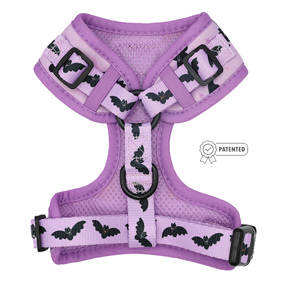 The Sassy Woof Dog Adjustable Harness - Lil Batty features a vibrant purple hue with a bat pattern, black buckles, and a central D-ring for easy leash attachment. This spooky-season accessory includes an adjustable fit and displays Sassy Woof’s patented badge on the right side.