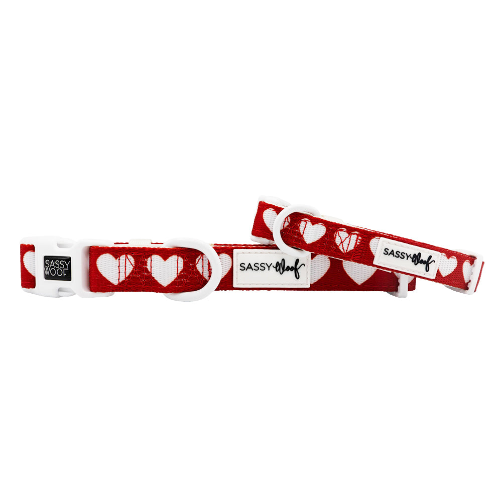 Red dog collar with white heart patterns and 'Sassy Woof' branding on a white background