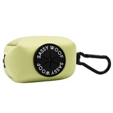 The Sassy Woof Dog Waste Bag Holder - Matcha is a light green rectangular neoprene pouch with a black circular "Sassy Woof" patch in white and features a black carabiner clip for easy attachment.