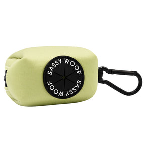The Sassy Woof Dog Waste Bag Holder - Matcha is a light green rectangular neoprene pouch with a black circular "Sassy Woof" patch in white and features a black carabiner clip for easy attachment.