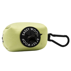 The Sassy Woof Dog Waste Bag Holder - Matcha is a light green neoprene holder with a black round label, black carabiner, and center waste bag dispenser—perfect to pair with an adjustable harness.