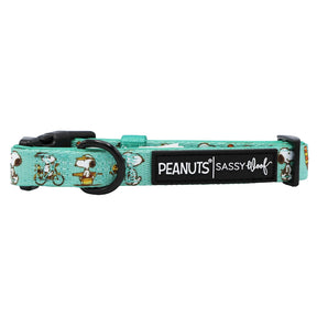 The Sassy Woof Dog Collar - Peanuts™ Road Trippin' is a turquoise, adjustable collar with Snoopy illustrations, black buckle, metal ring, and a black PEANUTS | SASSY WOOF label—ideal comfy adventure gear for your dog.