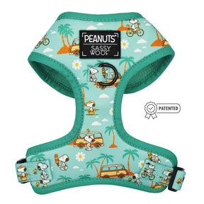 The Sassy Woof Dog Adjustable Harness - Peanuts™ Road Trippin' is a teal harness with Snoopy, Woodstock, palm trees, vans, bikes, and flowers. It features a logo patch, metal leash ring, and patented badge.