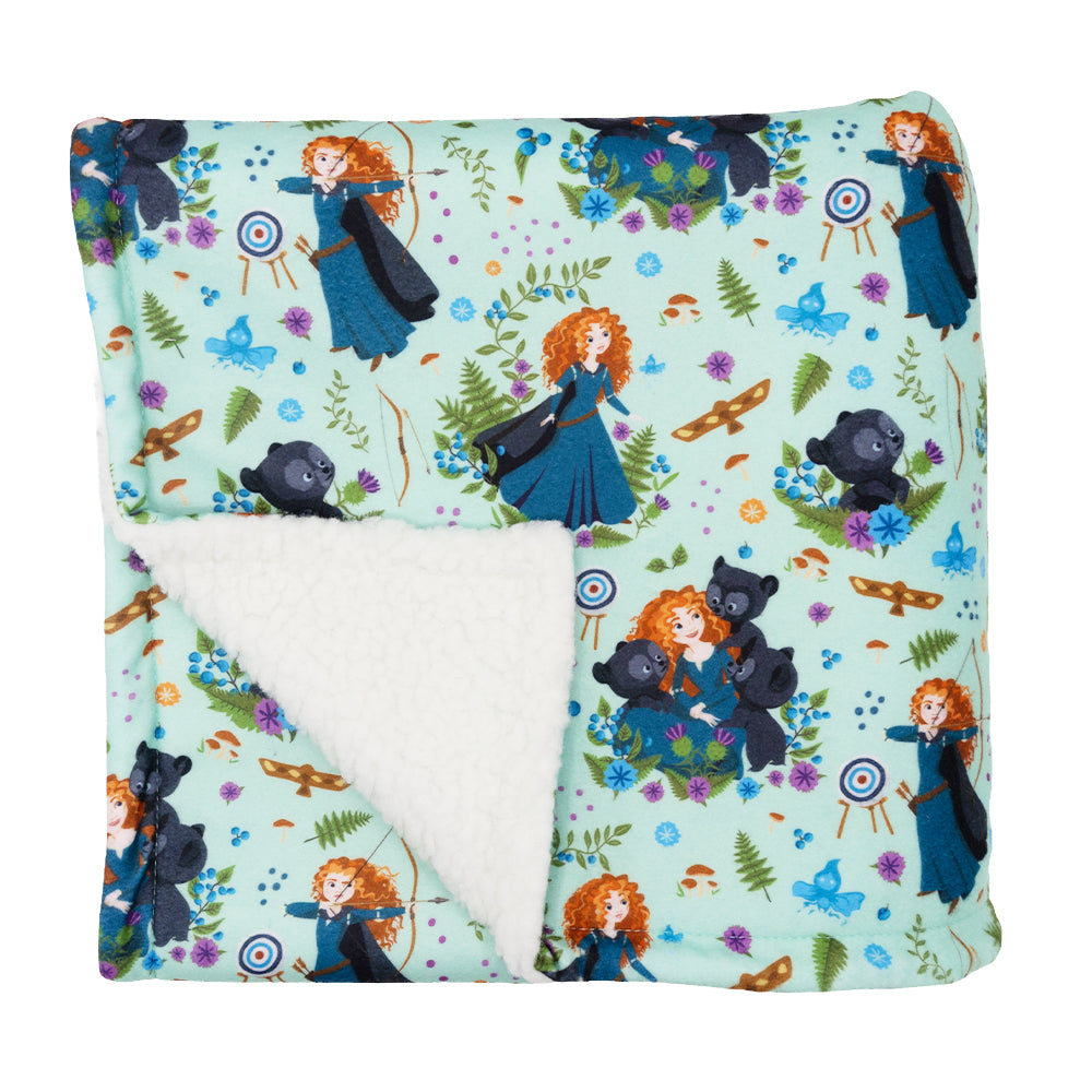 The Sassy Woof Pet Blanket - Disney's Merida is a soft sherpa dog blanket, featuring Merida in a blue dress, bears, archery targets, and forest designs. One corner folds to show the plush white lining—ideal for cozy comfort.
