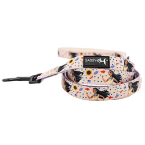 The Dog Two Piece Bundle - Disney's Pocahontas by Sassy Woof is a rolled-up leash with a light pink background, decorated with women with long dark hair, sunflowers, colorful dots, a black clasp, and a Sassy Woof label.