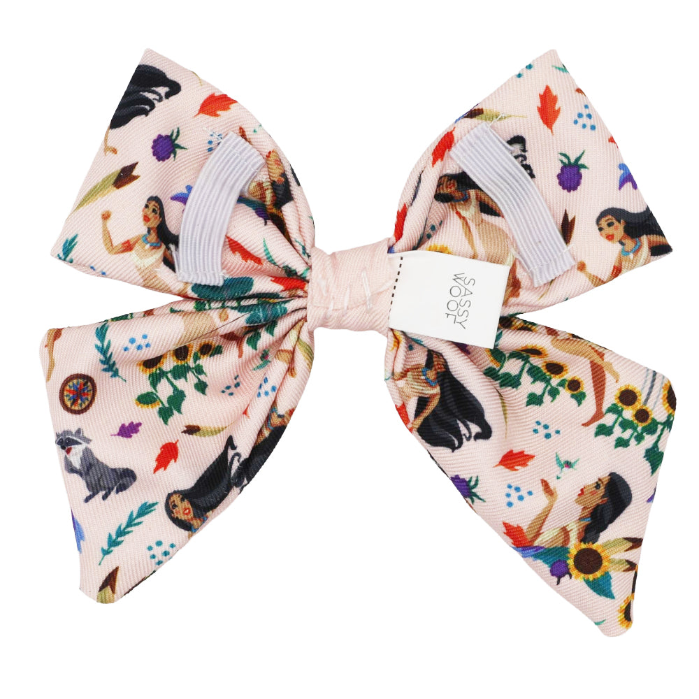 The Sassy Woof Dog Sailor Bow - Disney's Pocahontas features a pale pink backdrop with vibrant illustrations of women, animals, leaves, sunflowers, and more—perfect for pairing with adventurous dog accessories. Sassy Woof tag at the center.