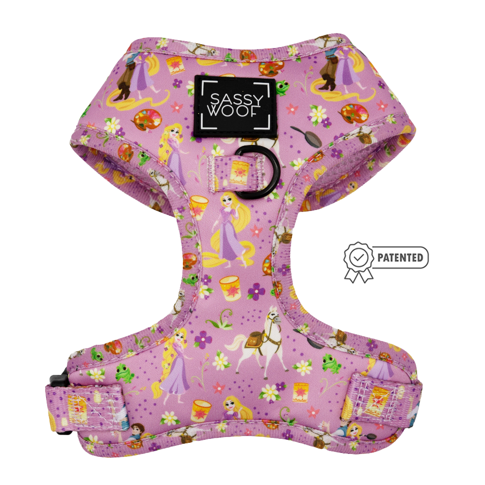 The Sassy Woof Dog Adjustable Harness – Disney's Rapunzel features a Tangled-inspired pink print with Rapunzel, Pascal, lanterns, and flowers, plus a black brand patch, back metal leash ring, and patented icon on the right.
