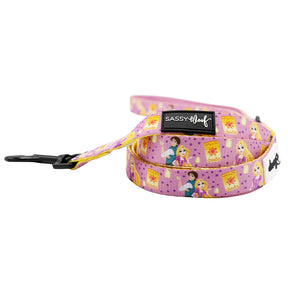 The Sassy Woof Dog Leash - Disney’s Rapunzel is pink with cartoon princess designs, yellow accents, a black metal clasp, and a Sassy Woof label. Pair it with matching Disney accessories like an adjustable harness or collar.