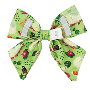 The Dog Sailor Bow - Disney's Tiana by Sassy Woof is a green fabric hair bow with a floral and Tiana print, featuring girl and flower images. Two white elastics and “Sassy” label included. Pairs perfectly with any Disney dog harness.