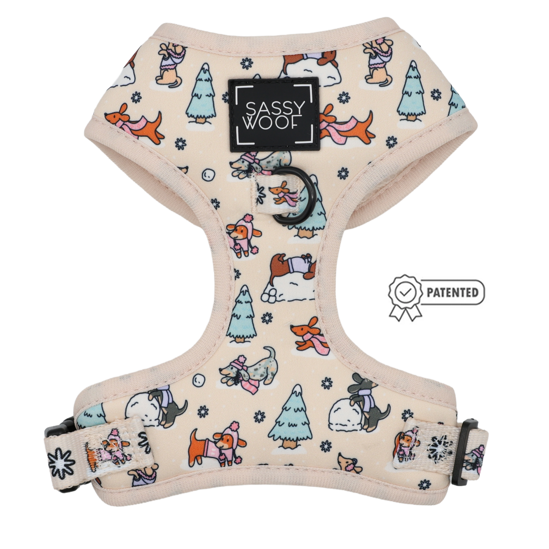Introducing the Dog Adjustable Harness - Weenie Wonderland by Sassy Woof: a beige harness adorned with a whimsical winter dog and tree pattern, featuring adjustable straps for an ideal fit. It showcases a front label reading “Sassy Woof” and displays a patented badge with ribbon icon on the side, making it an essential addition to your winter dog accessories collection.