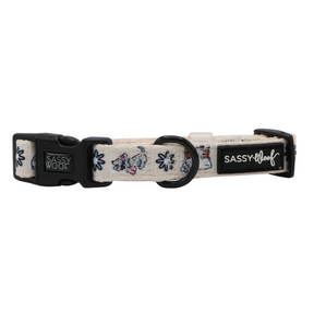 Introducing the Sassy Woof Dog Four Piece Bundle from the Weenie Wonderland Collection: a light-colored dog collar adorned with charming small dog and leaf illustrations, featuring a black buckle and D-ring. The collar displays Sassy Woof branding on two black tags and can be perfectly paired with the matching adjustable harness for a coordinated look.
