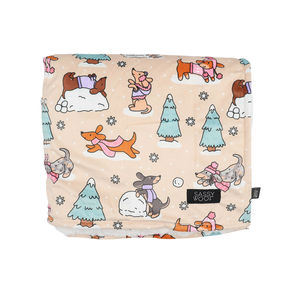 Snuggle up your pup with the Sassy Woof Pet Blanket - Weenie Wonderland: a beige blanket adorned with playful cartoon dogs in sweaters surrounded by snow, trees, and snowflakes—perfect for capturing the cozy charm of winter. The signature Sassy Woof brand tag is featured on the fabric.