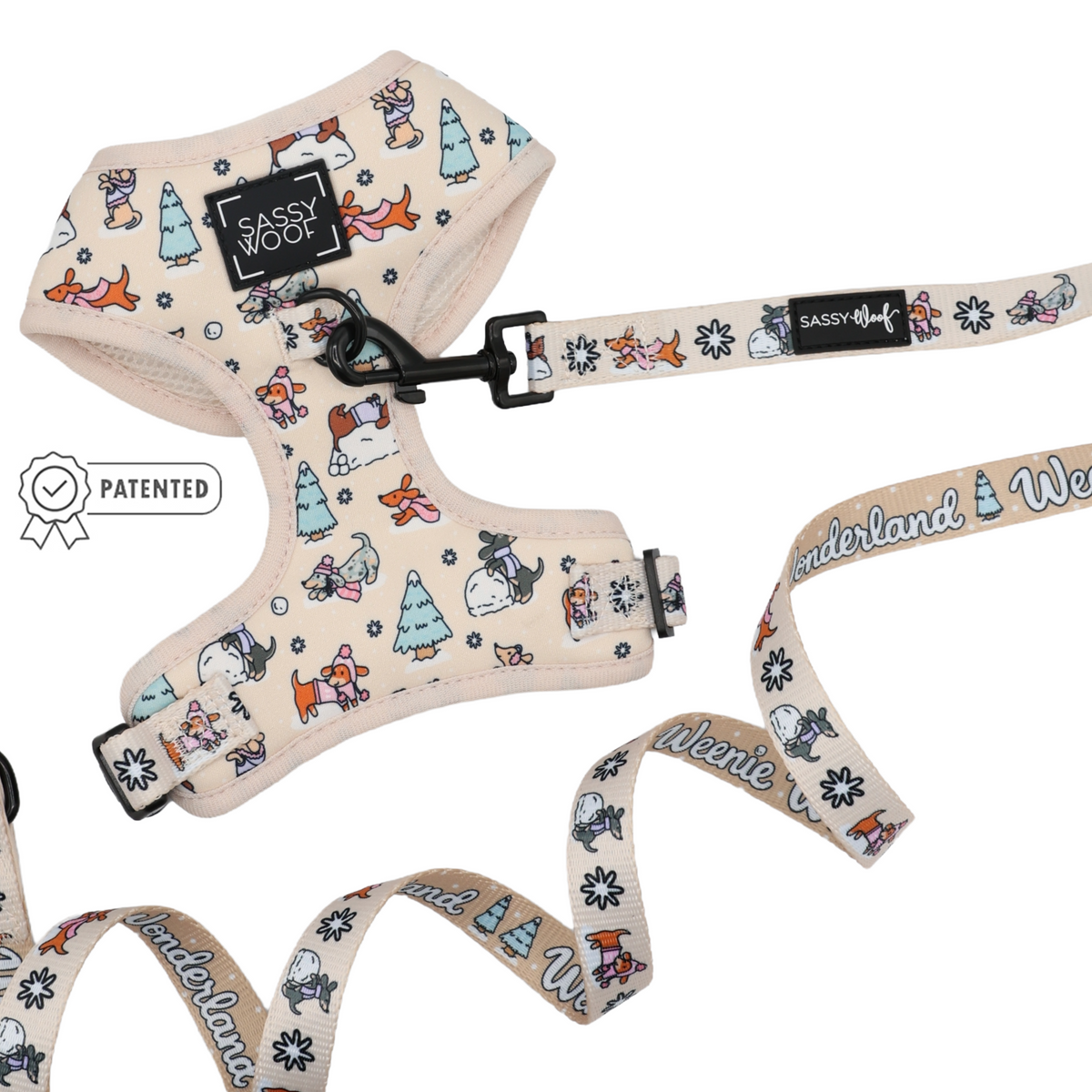 The Sassy Woof Dog Two Piece Bundle – Weenie Wonderland features a cream-colored harness adorned with cartoon dogs, trees, and festive motifs. The winter dog harness displays a Sassy Woof logo patch, while the adjustable leash is inscribed with “Weenie Wonderland.” A Patented badge appears to the left.