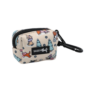 Here’s your rewritten sentence using the provided product data: The Dog Waste Bag Holder - Weenie Wonderland by Sassy Woof is a small, beige zippered pouch with a black clip, adorned with colorful illustrations of dogs, trees, and snowflakes. Part of the Weenie Wonderland Collection, this stylish accessory features a Sassy Woof label—perfect for carrying dog waste bags and dachshund winter essentials on your daily walks.
