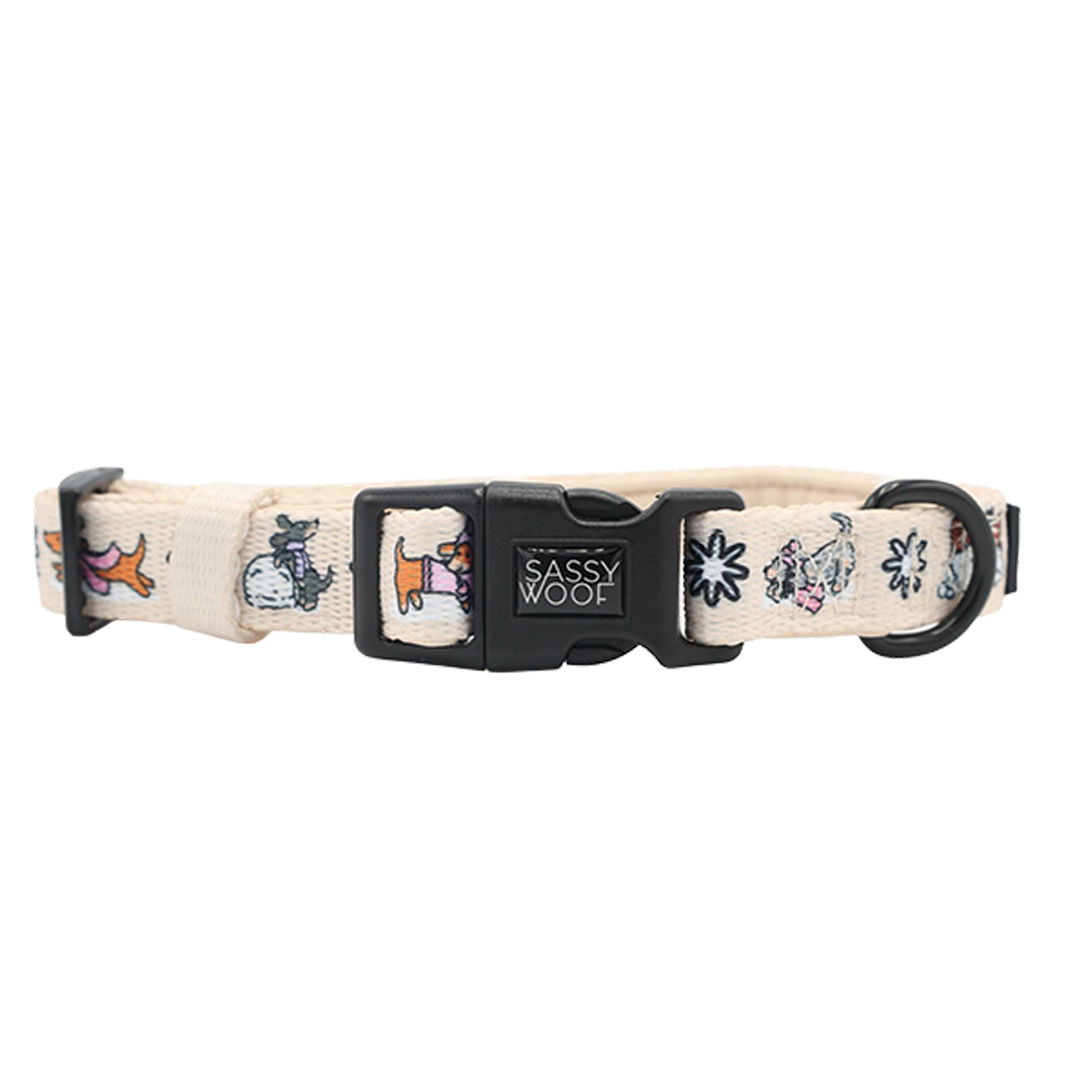 Introducing the Dog Collar - Weenie Wonderland by Sassy Woof—a beige adjustable dog collar decorated with playful cartoon dogs and floral patterns. This festive accessory features a sturdy black plastic buckle embossed with the Sassy Woof logo and a metal ring for easy leash attachment, making it perfect for stylish pups.
