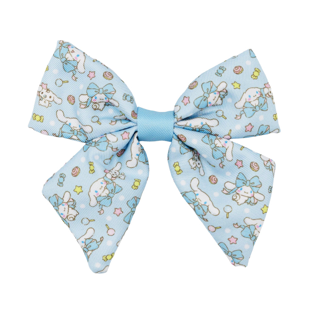 The Sassy Woof Dog Sailor Bow - Cinnamoroll™ is a light blue bow with a central knot, featuring playful Cinnamoroll, lollipops, stars, and candy designs in pastels. Perfect for pairing with Sanrio dog accessories. Shown on a white background.