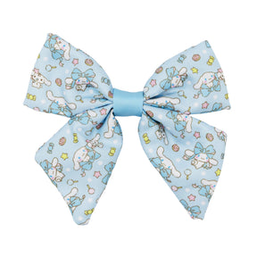 The Sassy Woof Dog Sailor Bow - Cinnamoroll™ is a light blue bow with a central knot, featuring playful Cinnamoroll, lollipops, stars, and candy designs in pastels. Perfect for pairing with Sanrio dog accessories. Shown on a white background.