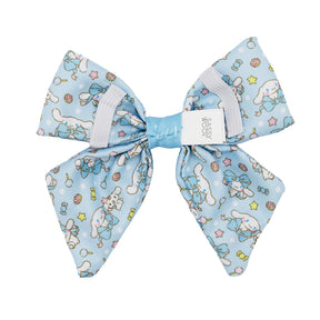The Dog Sailor Bow - Cinnamoroll™ by Sassy Woof features playful white Cinnamoroll characters, stars, and pastel sweets on light blue fabric with a white center clip—perfect for Sanrio dog accessory fans.