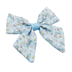The Sassy Woof Dog Sailor Bow - Cinnamoroll™ features a light blue fabric with white cartoon bunnies, yellow stars, and candy prints. Four wide loops and a central knot make it the perfect accessory for Cinnamoroll collection harnesses.