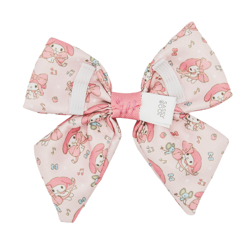 The Sassy Woof Dog Sailor Bow - My Melody™ is a pink dog bow with images of My Melody, music notes, and flowers. It features a white Sassy Woof tag and a pink center knot—perfect for Sanrio and Hello Kitty fans.