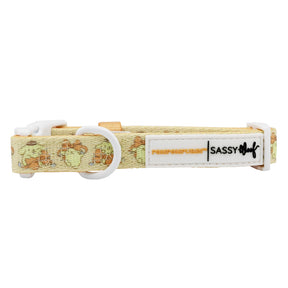 The Dog Collar - Pompompurin™ from Sassy Woof is a yellow adjustable collar with a cartoon sausage dog pattern, white plastic buckle, and a white "Sassy Woof" label—ideal for comfortable walks with your pup.