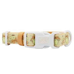 The Dog Collar - Pompompurin™ by Sassy Woof is beige and light green, with a white plastic buckle displaying the brand name, metal ring, and a subtle pattern featuring cartoon dogs.