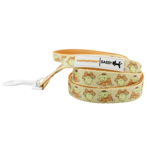 The Sassy Woof Collar Three Piece Bundle - Pompompurin™ features a playful yellow dog leash with repeating Pompompurin images, a white clip, and “SASSY WOOF” label—perfect for adding fun to your dog accessories collection.