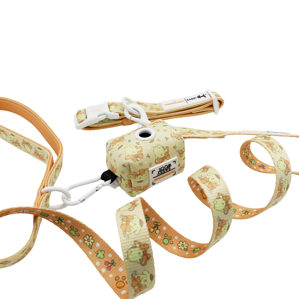 The Sassy Woof Collar Three Piece Bundle - Pompompurin™ features a beige leash with cartoon animal and flower prints, a matching waste bag dispenser, and a white plastic buckle, all displayed against a white background.
