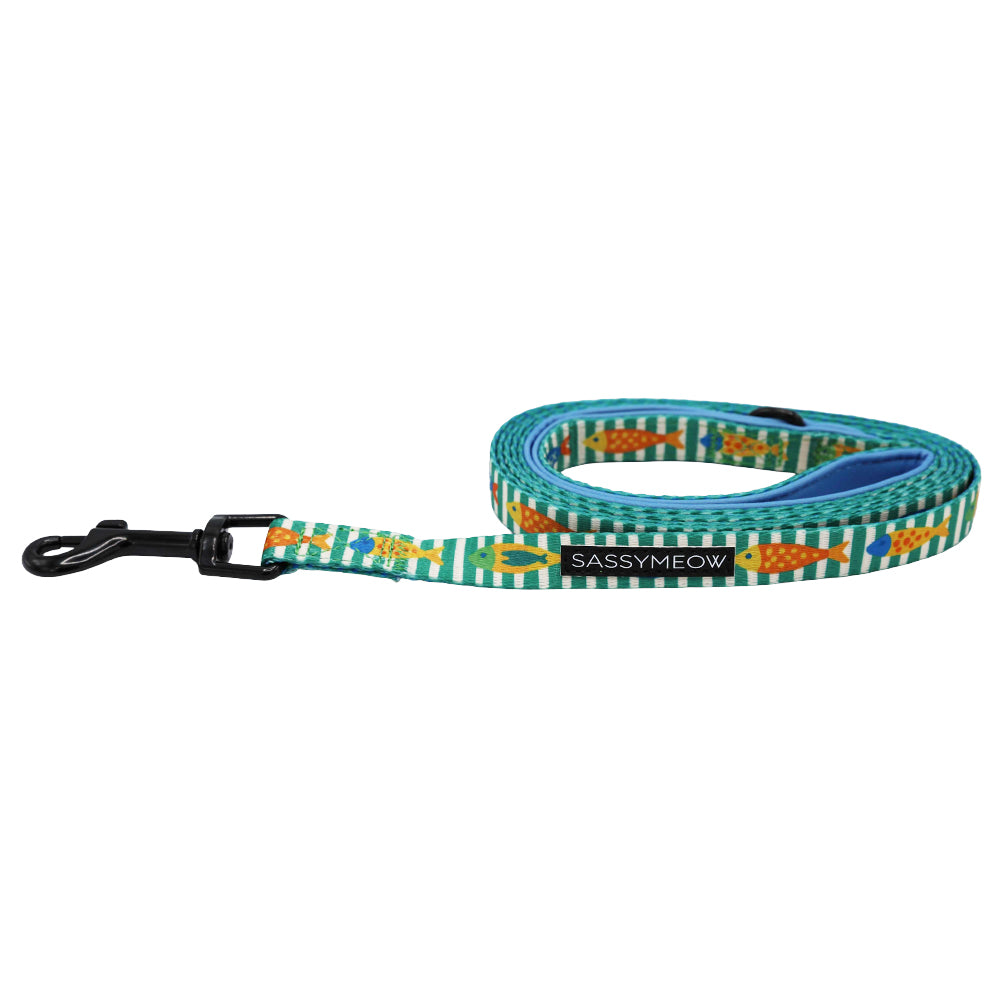 The Sassy Woof Cat Leash - Portofino features a green and white striped design with orange fish, a black metal clasp, and a SASSYMEOW label. The leash is from the Portofino collection and is shown coiled in a loose spiral.
