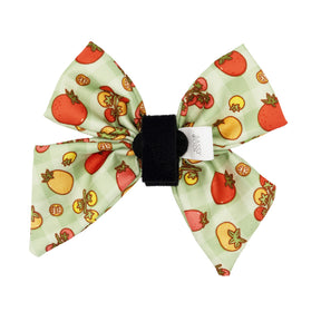 The Sassy Woof Dog Sailor Bow - Feeling Vine is a light green, plant-inspired fabric bow with colorful tomatoes, a black Velcro strap, and a white Sassy Woof tag—ideal to pair with an adjustable harness or matching leash.