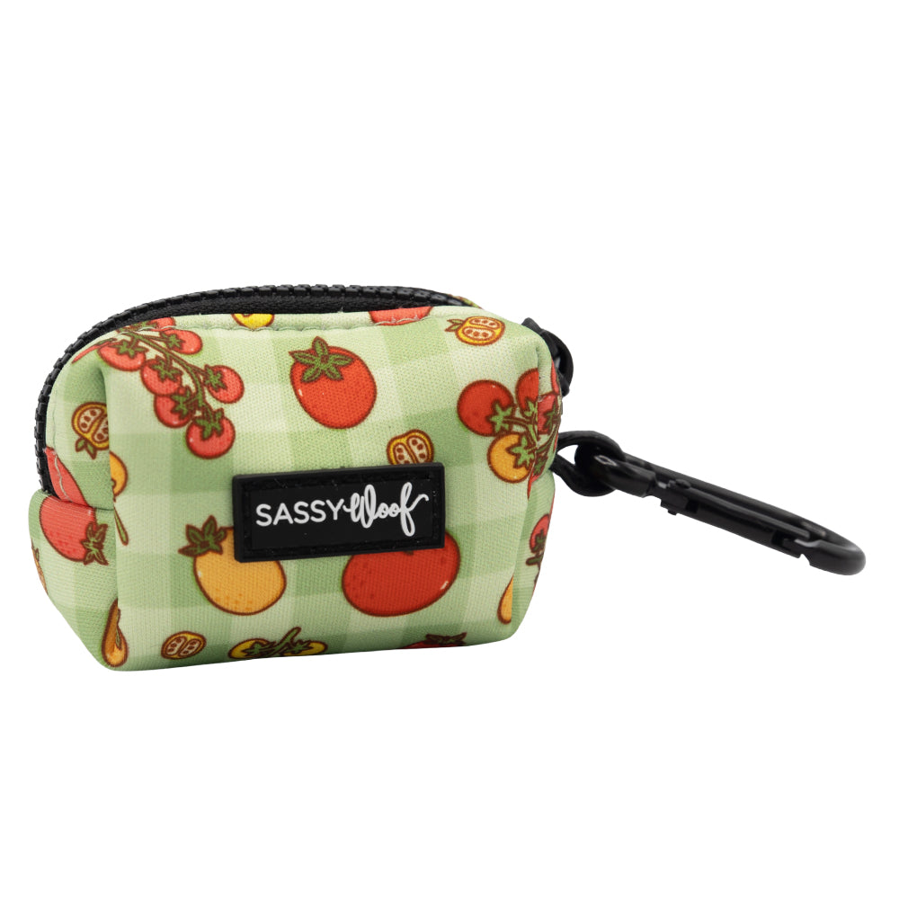 The Sassy Woof Dog Waste Bag Holder - Feeling Vine is a small green pouch with a black zipper, plant-inspired tomato illustrations, a Sassy Woof label, and a black clip for attaching to bags or leashes—perfect for waste bags.