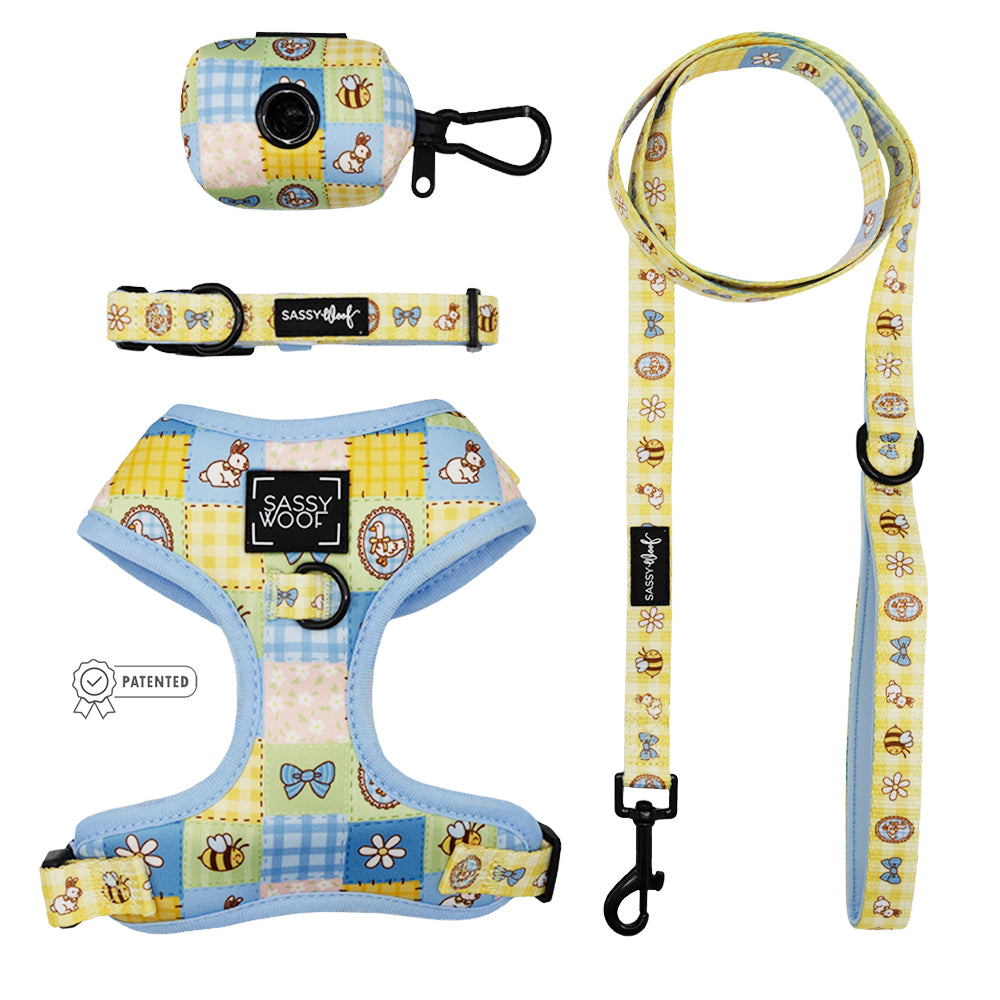 The Sassy Woof Dog Four Piece Bundle - Patch Perfect includes an adjustable harness, collar, leash, and waste bag holder with pastel patchwork of bees, butterflies, flowers & bears. All feature black hardware and Sassy Woof branding.