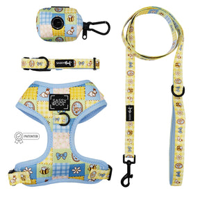 The Sassy Woof Dog Four Piece Bundle - Patch Perfect includes an adjustable harness, collar, leash, and waste bag holder with pastel patchwork of bees, butterflies, flowers & bears. All feature black hardware and Sassy Woof branding.