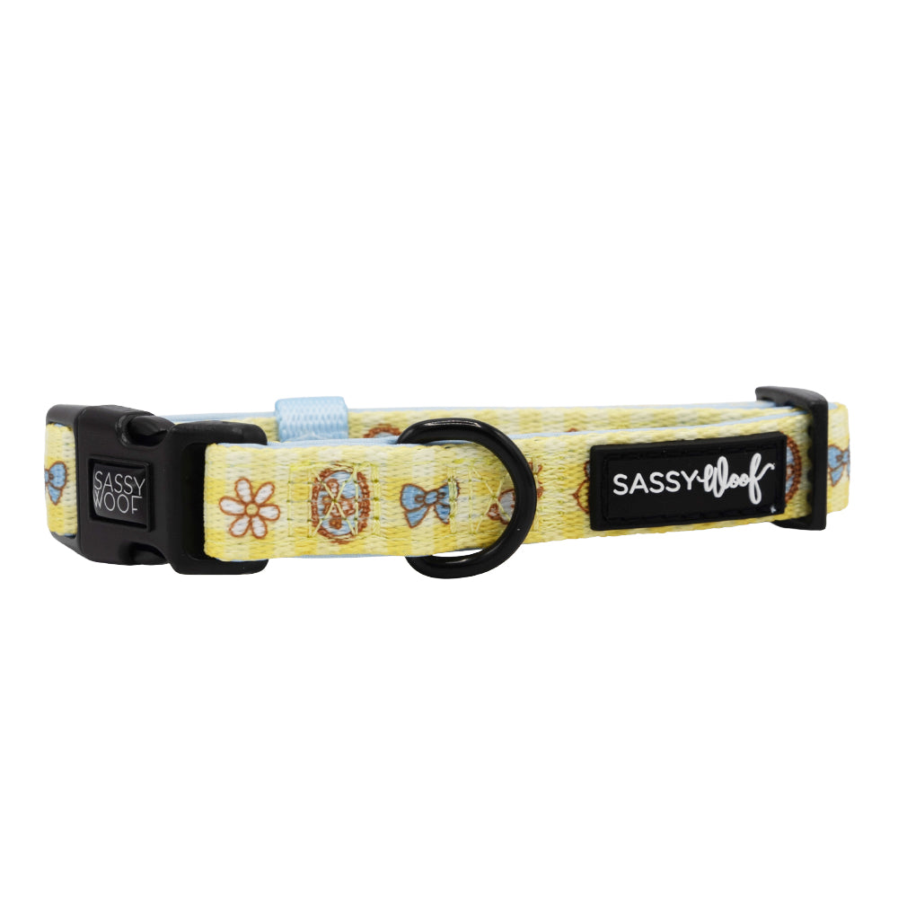 The Patch Perfect Dog Collar by Sassy Woof is a yellow adjustable collar with fun flower and bow designs, crafted from soft neoprene for comfort. It features a black buckle, ring for tags or leash, and a Sassy Woof label—ideal for growing pups.